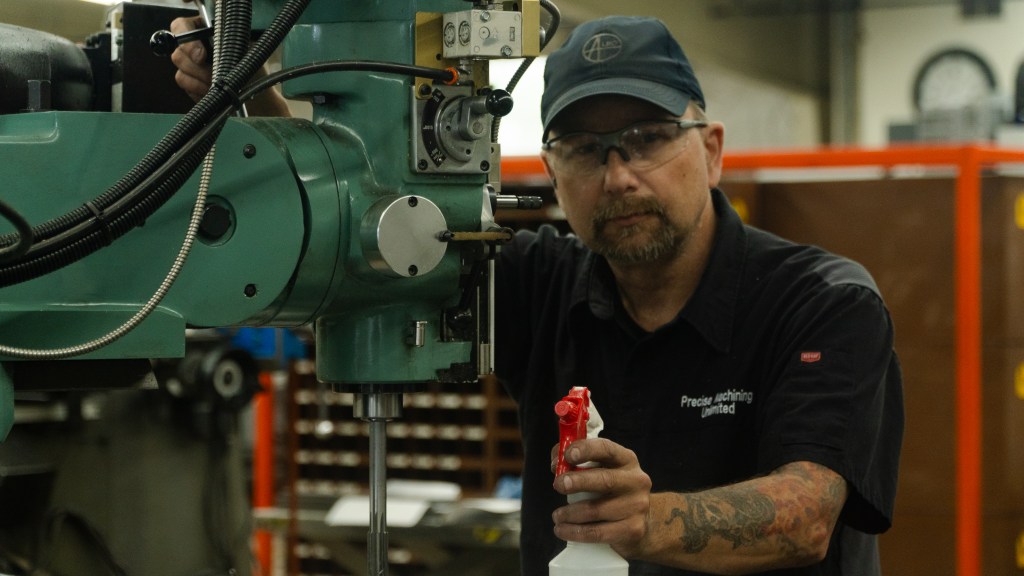 Close-up image of a machine shop worker smiling while operating machinery, capturing the essence of machine shop culture. The worker’s positive demeanor highlights the collaborative and skilled environment of the workshop. The image emphasizes the blend of professional craftsmanship and a supportive, engaging atmosphere in the industrial setting.