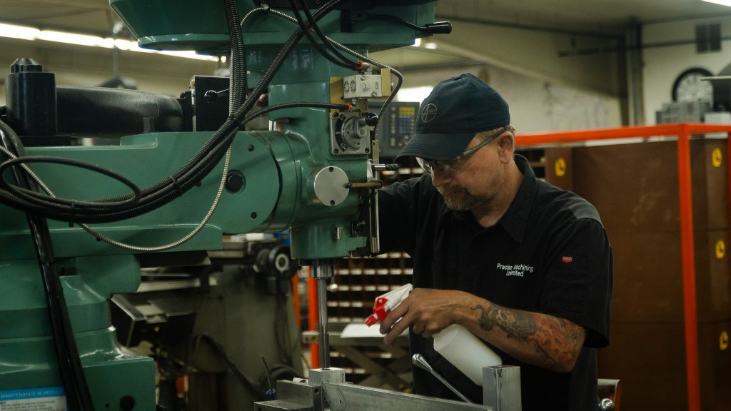 Close-up of a skilled technician operating a high-tech machine in a machine shop. The image highlights the technician’s hands adjusting the machine’s settings, emphasizing precision and expertise. The focus is on the advanced industrial equipment and the detailed, high-quality work being performed.